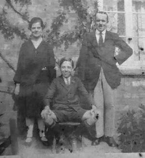 Parents (standing) and son (seated) in front of window of terraced house